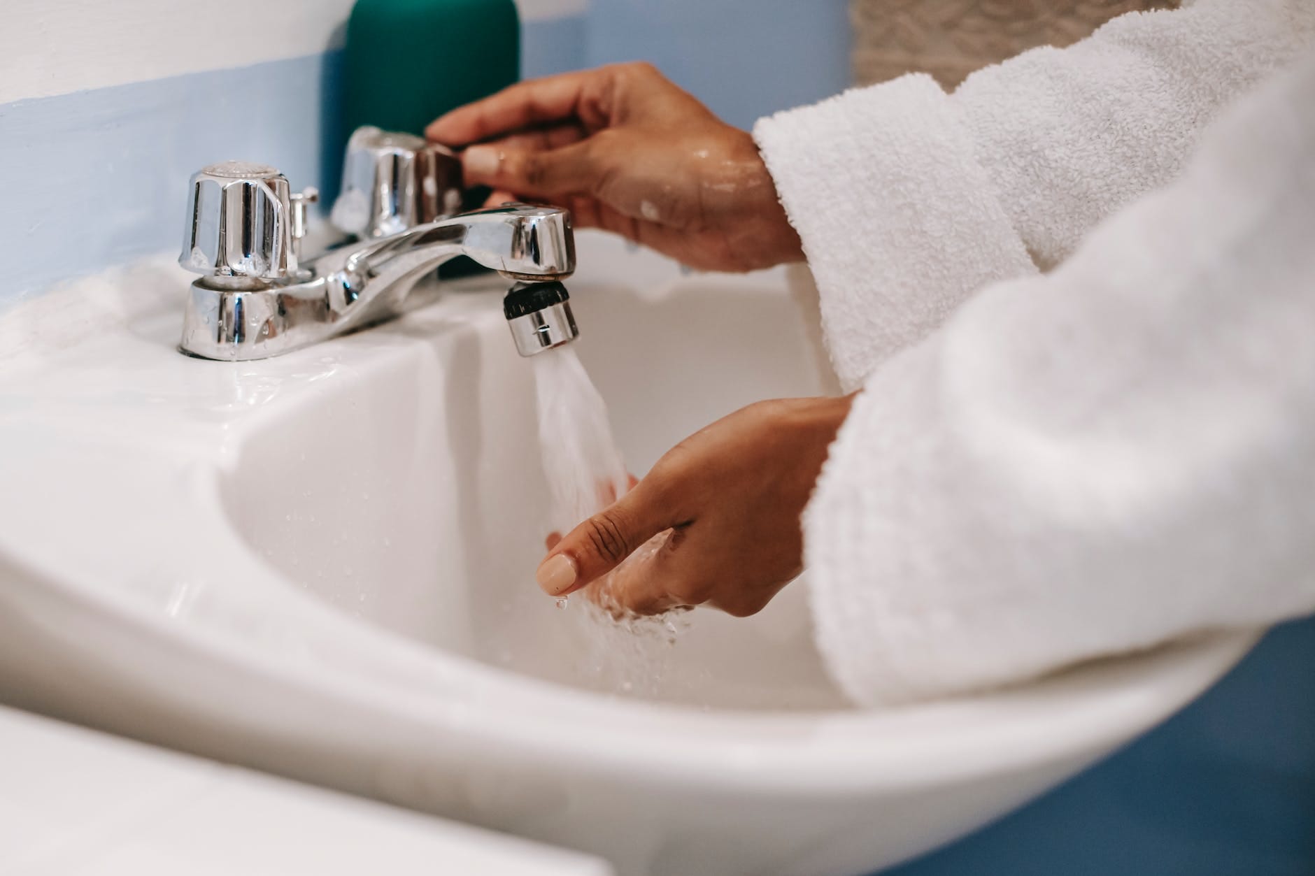 crop ethnic woman in robe washing hands in bathroom